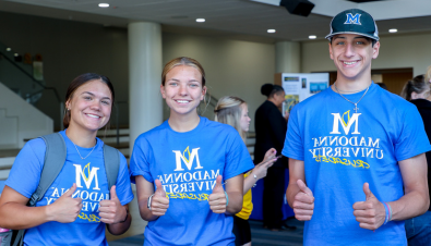 三名身穿圣母大学衬衫的学生在迎新会上对着镜头微笑